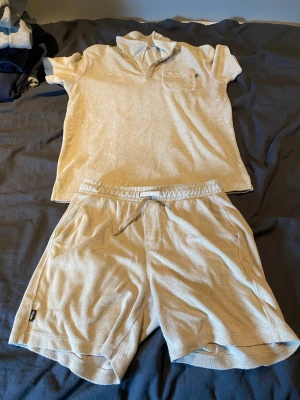 Beige set i frotté med krage - Säljer ett beige tvådelat set i mjuk frotté. Överdelen har korta ärmar, krage och bröstficka, medan shortsen har resårmidja med dragsko och sidofickor. Perfekt för en avslappnad och bekväm stil hemma eller på semestern skorsten är 146-152 tröjan 158-164.