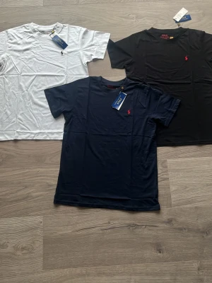 3-pack t-shirts från Polo Ralph Lauren - KAMPANJ! Säljer ett 3-pack klassiska t-shirts från Polo Ralph Lauren i färgerna vit, svart och marinblå. Alla har rund hals, korta ärmar och den ikoniska broderade loggan på bröstet. Perfekta basplagg i mjuk bomull för en clean och stilren look. Finns även i andra storlekar 