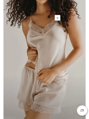 Beige sidenpyjamas med spetsdetaljer - Säljer ett set från intimissimi med pyjamas i beige siden med tunna axelband och fina spetsdetaljer vid halsringning och benslut. Shortsen har elastisk midja och matchande spetskant. Perfekt för en lyxig och bekväm känsla hemma. Helt nytt köpte fel färg. Prislappar kvar 