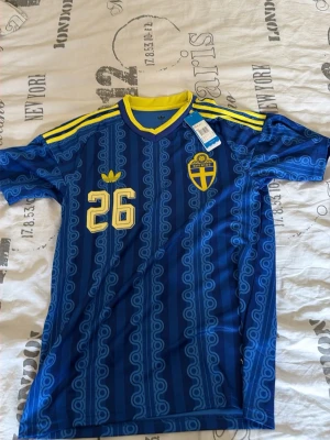 Blå Sverige fotbollströja Adidas - Säljer en blå Sverige fotbollströja från Adidas med nummer 26 i gult. Tröjan har gula detaljer på axlarna. Perfekt för dig som vill stötta Sverige på match eller ha till vardags. Pris går diskutera vid snabbt köpt, passar både M och S