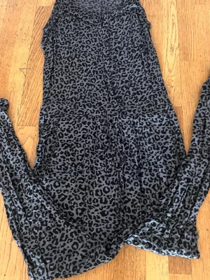 Leopardmönstrad ärmlös jumpsuit - Säljer en snygg ärmlös jumpsuit med leopardmönster i svart och grått. Jumpsuiten har knappar framtill och är tillverkad i ett mjukt, tunt material som känns skönt mot huden. Perfekt för dig som vill sticka ut med ett djurmönster!