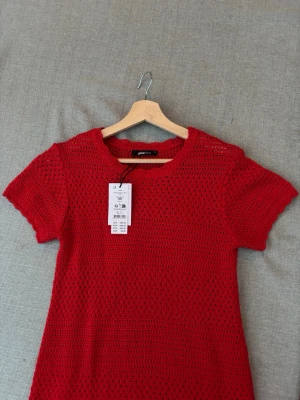 Röd stickad kortklänning - Snygg röd stickad klänning med kort ärm och rund halsringning. Klänningen har ett virkat mönster som ger en luftig känsla och passar perfekt till varmare dagar. Enkel och stilren design som är lätt att matcha med accessoarer. Köpt för 499 kr 