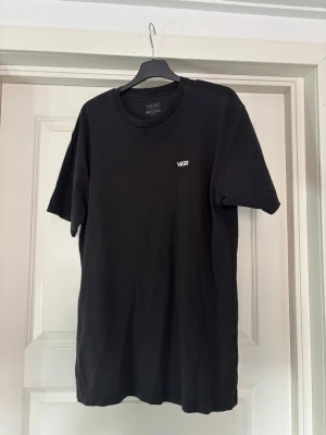 Svart t-shirt från Vans - Klassisk svart t-shirt från Vans i bomull med rund hals och korta ärmar. Diskret Vans-logga på bröstet. Perfekt basic-plagg för en avslappnad och stilren look.
