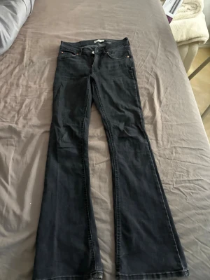 Svarta bootcut jeans - Säljer ett par svarta bootcut jeans med klassisk femficksdesign och utsvängda ben. Jeansen har normal midja och är tillverkade i ett mjukt denimtyg som sitter snyggt på kroppen. Perfekta för dig som gillar retrovibbar och en avslappnad stil.