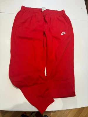 Röda mjukisbyxor från Nike - Snygga röda mjukisbyxor från Nike med klassisk logga på vänster ben. Nya oanvända 