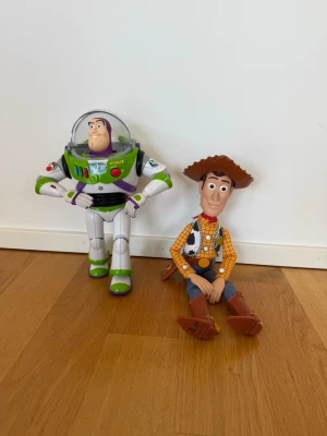 Buzz Lightyear och Woody figurer - Säljer två coola Toy Story-figurer: Buzz Lightyear i vit, grön och lila plastdräkt med hjälm och detaljer samt Woody med cowboyhatt, skjorta och boots. Perfekta för samlare eller som dekoration i rummet!