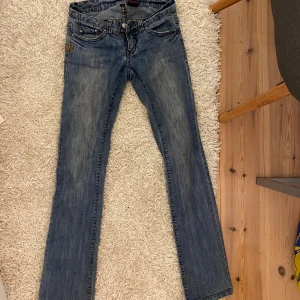 Blå jeans med broderad bakficka - Säljer ett par snygga blå jeans med en cool broderad detalj på bakfickan. De har en klassisk femficksdesign och är i en straight passform. Perfekta för vardagsbruk och kan enkelt matchas med olika toppar. Vintedjeans från bikbok