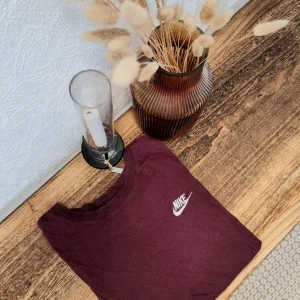Vinröd t-shirt från Nike - Säljer en snygg vinröd t-shirt från Nike. Den är i bomull och har en normal passform med korta ärmar. Nike-loggan är tryckt i vitt på bröstet. Skön och stilren!