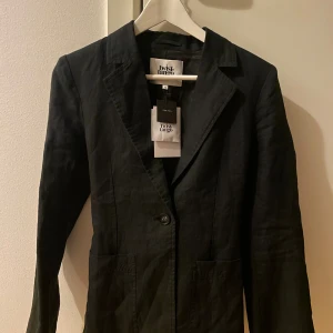 Linnekavaj Twist & Tango - Snygg svart 100% linnekavaj med skärp i midjan. Kavajen har en enkel design med två fickor framtill och en knappstängning. Prislappen kvar, aldrig använd. Originalpris 2499kr.