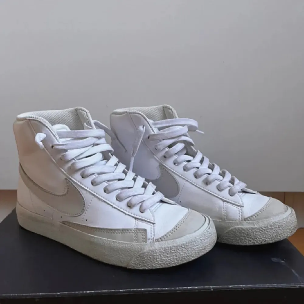 Säljer ett par vita Nike sneakers i nyskick. De har en klassisk hög design med snörning och en diskret Nike-logga på sidan. Perfekta för både vardag och festliga tillfällen. Skorna är bekväma och stilrena, vilket gör dem lätta att matcha med olika outfits.. Skor.