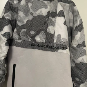 Grå och vit camouflagejacka från BlackSquad - Säljer en supercool grå och vit camouflagejacka från BlackSquad. Den har en unik design med ett snyggt mönster och en dragkedja framtill. Perfekt för höst och vår när du vill sticka ut lite extra. Jackan är långärmad och har en normal passform. Den är i nyskick och redo för nya äventyr!