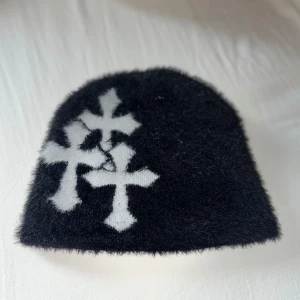 Svart mössa med vita kors - Säljer en svart mössa med tre vita kors på framsidan. Den är supermjuk och perfekt för kalla dagar. Mössan har en enkel och stilren design som passar till det mesta. Perfekt för både höst och vinter!