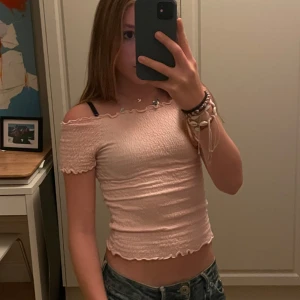 Rosa offshoulder topp - Säljer en superfin rosa offshoulder topp i ett stretchigt och ribbat material. Toppen har korta ärmar och en söt volangdetalj vid kanterna. Perfekt för sommardagar eller en avslappnad festkväll. Passar bra med jeans eller kjol!