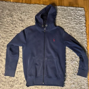 Blå hoodie från Ralph Lauren - Säljer en snygg blå hoodie från Ralph Lauren med dragkedja och huva. Passar dej som är 170-175