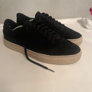 Svarta mocka skor från Vagabond - Snygga svarta mocka skor från Vagabond med en stilren design. Skorna har en ljus beige sula och är tillverkade i mocka med snörning framtill. Perfekta för en avslappnad stil.