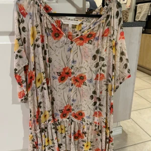 Blommig tunika  från Pernilla Wahlgren - Charmig blommig klänning från Pernilla Wahlgren i en luftig design. Klänningen har en v-ringad hals och trekvartsärmar, perfekt för vår och sommar. Den har ett färgglatt mönster med röda, gula och blå blommor på en ljus bakgrund.