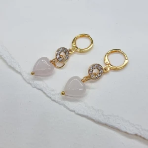 Guldörhängen med hjärtformade hängen - Silver925.Eleganta guldörhängen med glittrande detaljer och hjärtformade hängen i ljusrosa. Perfekta för att ge en romantisk touch till din stil.