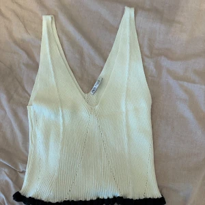 Vit ribbad topp från Zara - Snygg vit ribbad topp från Zara med v-ringning och svarta detaljer vid nederkanten. Helt oanvänd 