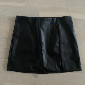Svart skinnkjol - Snygg svart skinnkjol i kort modell. Perfekt för en trendig look med en stilren design. Kjolen har en slät yta och en klassisk passform.