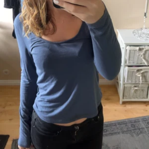 Blå långärmad topp - Säljer en stilren blå långärmad topp med en djupare rund halsringning. Perfekt för en avslappnad look. Passar bra till jeans eller kjol.