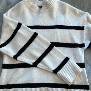  stickad tröja - Snygg vit stickad tröja med svarta ränder. Tröjan har långa ärmar och en rund halsringning. Perfekt för en stilren look. Aldrig andvänd och skov för fler bilder eller frågor💞