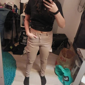 Beige cargopants med fickor - Snygga beige cargopants med flera praktiska fickor och en tight passform. Byxorna har en modern design med dragkedja och knappar framtill. Perfekta för en avslappnad stil.