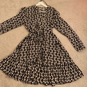 Mönstrad omlottklänning - Snygg omlottklänning med svart och vitt mönster. Klänningen har långa ärmar och ett knytband i midjan. 