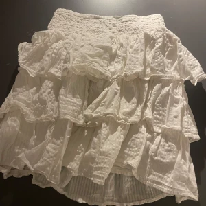 Vit volangkjol - Charmig vit kjol med flera lager av volanger. Perfekt för en somrig look med sin luftiga design och elastiska midja för bekväm passform.