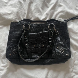 Svart märkesväska från Stockh LM - Snygg vintage svart axelväska i krokodilmönstrat skinn från Stockh LM. Väskan har flera detaljer som dragkedja och spännen i silverfärg. Den ser lite sliten ut men det är bara del av designen så är igentligen i bra skick💕