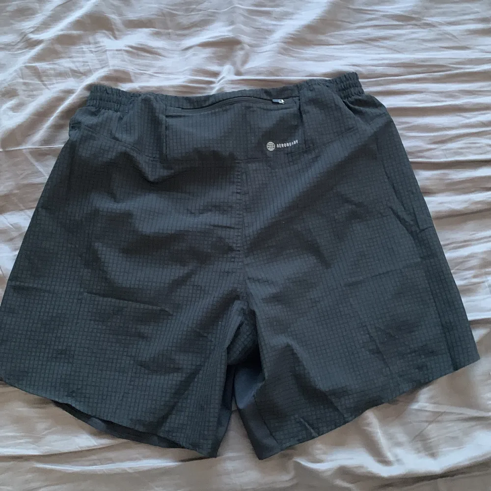 Säljer ett par svarta träningsshorts från Adidas, tillverkade av Parley Ocean Plastic. Shortsen har en elastisk midja och vita detaljer på sidorna. Perfekta för löpning med AEROREADY-teknologi för att hålla dig torr och bekväm.. Sportswear.