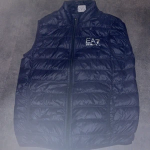 Svart väst från EA7 - Snygg svart dunväst från EA7 med dragkedja framtill. Perfekt för lager-på-lager under kyliga dagar. Västen har en stilren design med EA7-logga på bröstet