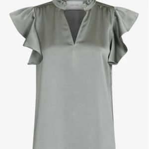 Grön blus från Neo Noir - Snygg grön blus från Neo Noir i ett glansigt material. Blusen har volangdetaljer vid ärmarna och en v-ringad hals. Perfekt för en stilren look. Toppen är i princip oanvänd och det finns inget tecken på användning, nypris 600kr, mitt pris 400💖