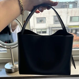 Svart handväska från Arket - Arket väska ( den stora modellen). Mycket bra skick. Det finns ett tillhörande längre band til väskan. Nypris 1990 kr. 