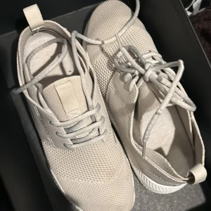 Beige sneakers från Boss - Snygga beige sneakers från Boss med snörning och en stilren design. Skorna har en kombination av mesh och syntetmaterial för en modern look. Perfekta för en avslappnad stil.