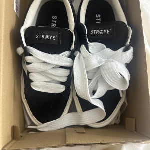 Svarta sneakers från Straye - Säljer ett par svarta sneakers från Straye med vita detaljer och snörning. Skorna har används en gång och är i super skick. Säljer då de tyvärr inte passar. Köpta för 1,400kr