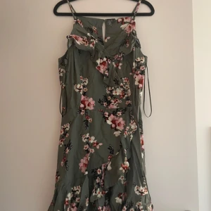 Blommig klänning från Rainbow - Säljer en vacker blommig klänning från Rainbow i grönt med rosa och vita blommor. Klänningen har smala axelband och volangdetaljer framtill. Perfekt för sommarens alla tillfällen!