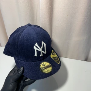 New Era keps - Snygg mörkblå keps från New Era med broderad vit logotyp på framsidan. Kepsen har en klassisk 59FIFTY design och är tillverkad i ett ribbat material. Perfekt för att ge en sportig touch till din outfit.