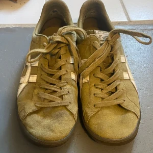 Gröna sneakers från Onitsuka Tiger - Säljer ett par gröna sneakers från Onitsuka Tiger med vita detaljer och snörning. Skorna har en klassisk design med låg profil och är perfekta för en avslappnad stil.