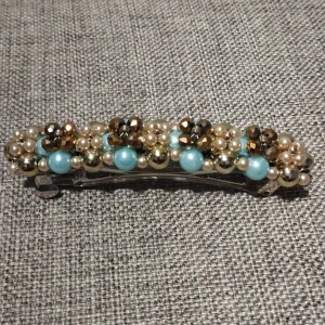 Hårspänne med pärlor och stenar - Elegant hårspänne dekorerat med pärlor i turkos och guld samt glittriga stenar. Perfekt för att ge en extra touch till din frisyr.