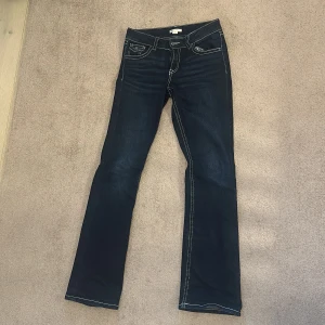 Mörkblå bootcut jeans från Gina Tricot - Snygga mörkblå bootcut jeans från Gina Tricot med kontrasterande vita sömmar. Klassisk femficksdesign med dragkedja och knapp framtill. Perfekta för en stilren look.
