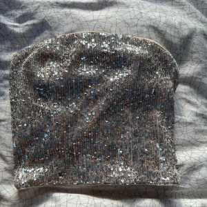 Glittrig tubtopp från H&M - Snygg glittrig tubtopp från H&M i silver med paljetter. Perfekt för en festlig kväll. Toppen har en dragkedja bak för enkel på- och avtagning. Aldrig använd med prislappen kvar 