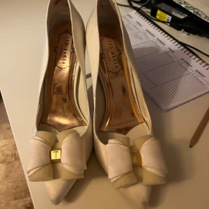 Vita pumps från Ted Baker - Vita högklackade skor från Ted Baker med rosetter fram. Perfekta för speciella tillfällen. Köpta från sellpy 