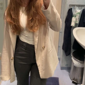 Beige kavaj från H&M - Elegant beige kavaj från H&M i storlek 36. Kavajen har en klassisk design med två knappar framtill och en stilren krage. Perfekt för att ge en sofistikerad touch till din outfit.