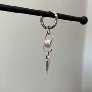 Silverörhänge i rostfritt stål med pärldetalj i  - Stilrent silverörhänge med en hängande pärla och en spetsig detalj. Perfekt för att ge en edgy touch till din look. Örhänget har en enkel ringdesign som gör det lätt att bära.