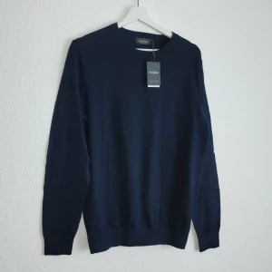 Mörkblå tröja från Dressmann - Säljer en stilren mörkblå tröja från Dressmann i Supima bomull. Tröjan har en klassisk design med långa ärmar och rund halsringning. Perfekt för en elegant och bekväm look.
