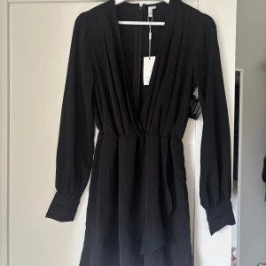 Svart klänning från Nelly - Snygg svart klänning från Nelly med djup v-ringning och långa ärmar. Aldrig använd
