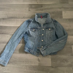 Blå jeansjacka från H&M - Säljer en blå jeansjacka från H&M. Jackan har en normal passform med långa ärmar och knappar framtill. Jackan är i bra skick, inga tecken på användning. Säljer för 100kr