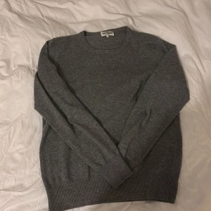 Grå kashmirtröja från Soft Goat - Säljer en elegant grå kashmirtröja från Soft Goat. Tröjan har en klassisk rund hals och långa ärmar, perfekt för kyligare dagar. Den är mjuk och bekväm, vilket gör den till ett måste i garderoben. Passar utmärkt för både vardag och mer uppklädda tillfällen. Har tunnare kashmir på höger armbåge som gör så att det syns igenom lite. Men märks inte av vid användning 