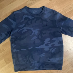 Blå camouflagemönstrad tröja från Polo Ralph Lauren - Säljer en blå camouflagemönstrad tröja från Polo Ralph Lauren. Tröjan har en rund halsringning och långa ärmar. Perfekt för en avslappnad stil. Riktigt skön samt unik!