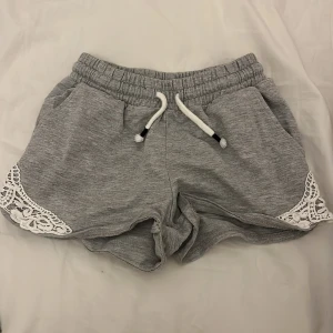 Grå shorts med spetsdetaljer - Snygga grå shorts med elastisk midja och snörning. De har fina spetsdetaljer på sidorna som ger en extra touch. Perfekta för en avslappnad stil.